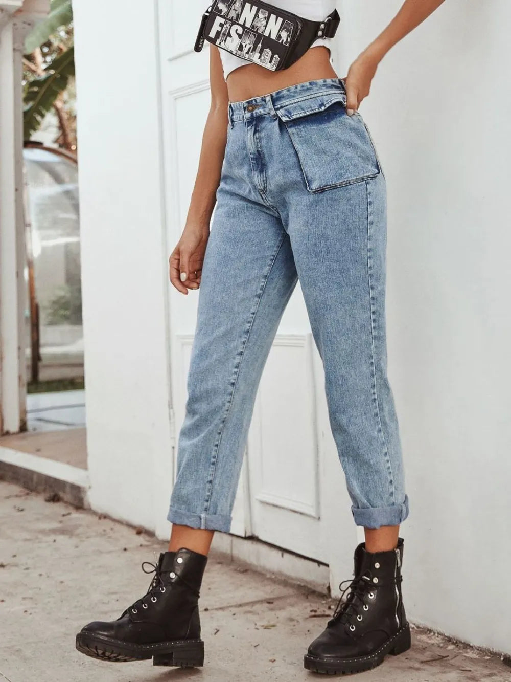 Person wearing light blue jeans and black boots standing against a white wall.