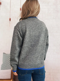 Person wearing a gray sweater with blue trim in a room setting