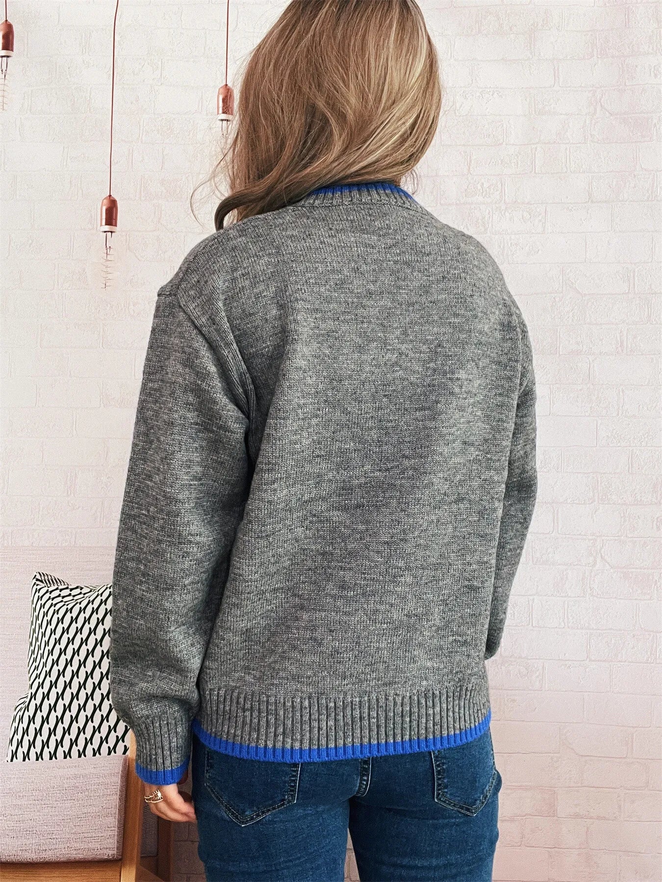 Person wearing a gray sweater with blue trim in a room setting