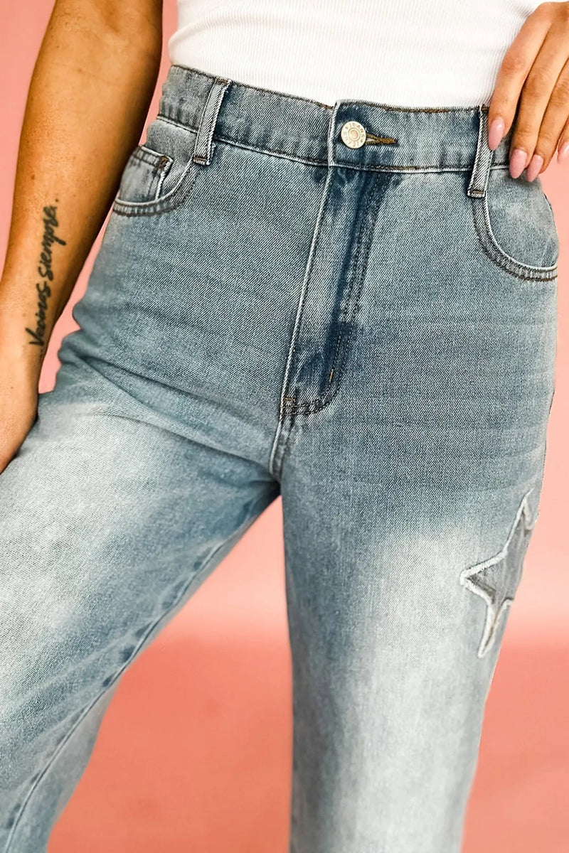 Close-up of light blue jeans with a star patch on a pink background
