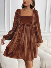 Woman wearing a brown pleated dress against a white wall.