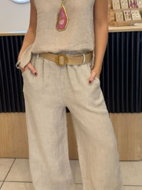 Person wearing a beige sleeveless top and wide-leg pants with a belt, standing indoors.