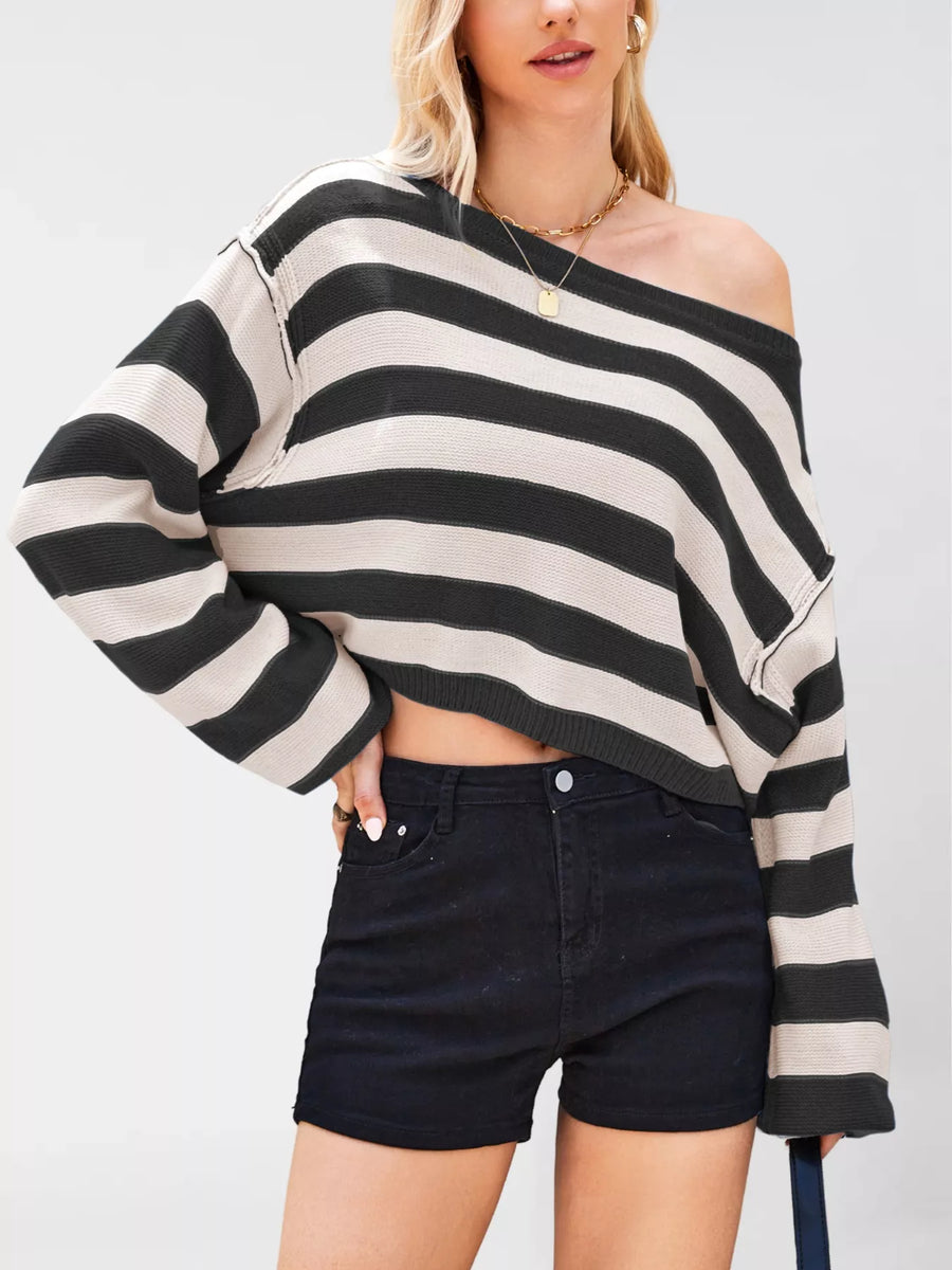Person wearing a black and white striped off-shoulder sweater with black shorts on a plain background