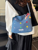 Person holding a blue bag with colorful embellishments in an indoor setting