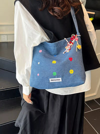 Person holding a blue bag with colorful embellishments in an indoor setting