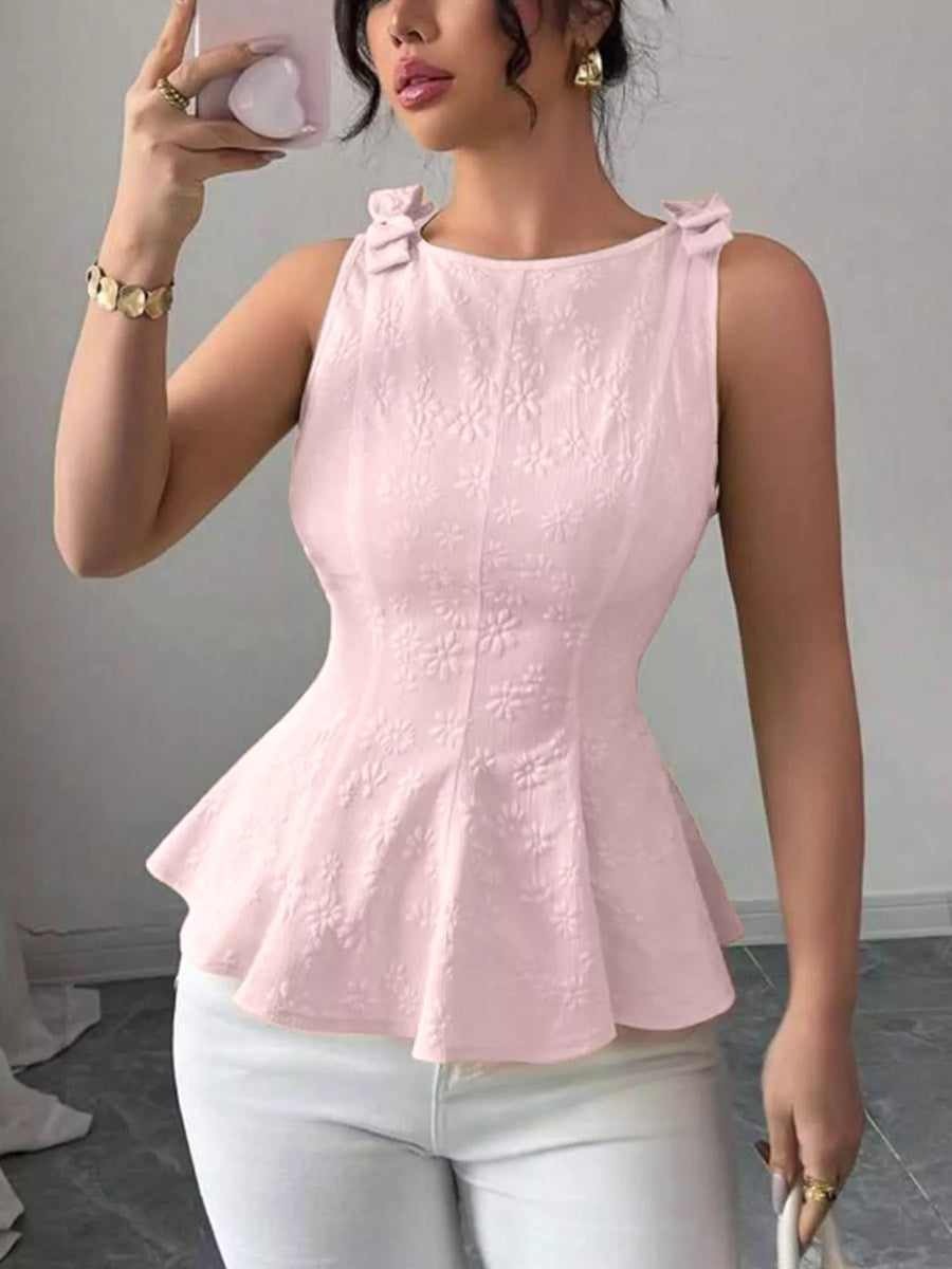Woman wearing a pink peplum top and white pants, taking a mirror selfie.