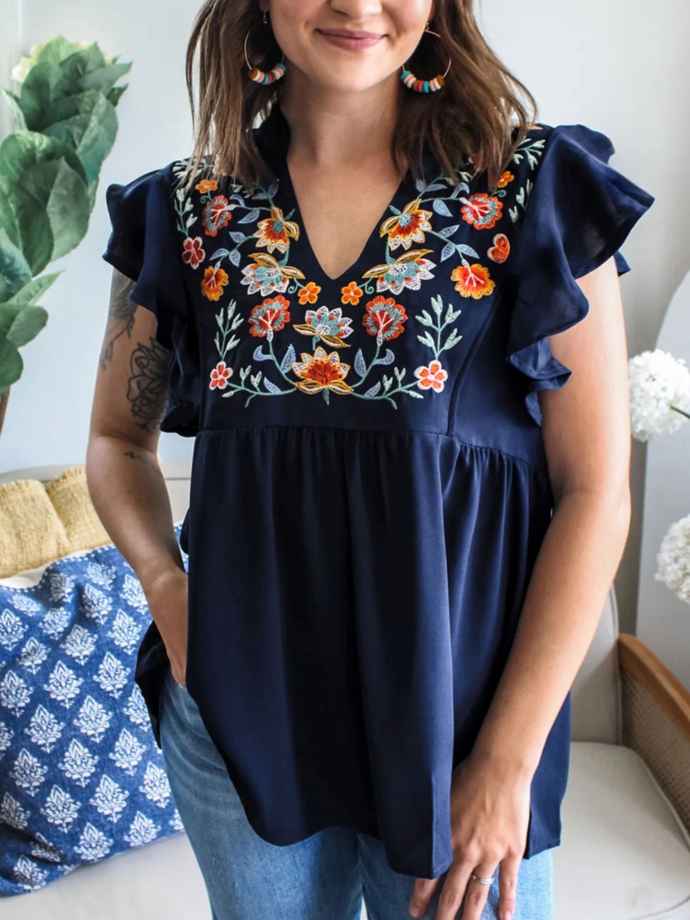 Woman wearing a navy blue blouse with floral embroidery in a home setting