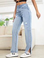 Person wearing light blue jeans with a slit, standing in a room with a couch and plants.