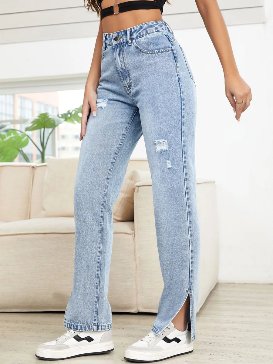 Person wearing light blue jeans with a slit, standing in a room with a couch and plants.