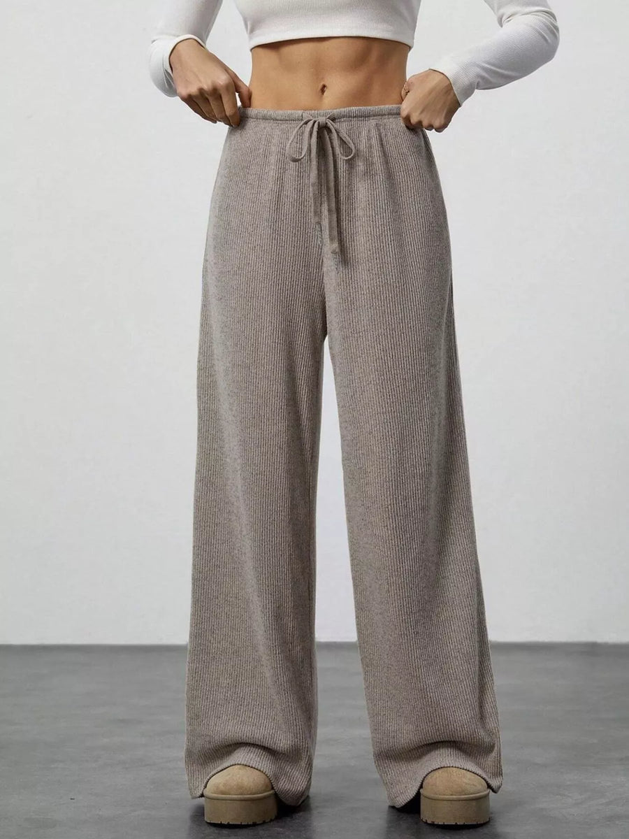 Person wearing brown wide-leg pants with a white top on a plain background