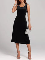 Woman wearing a black sleeveless dress holding a silver clutch against a plain background