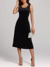 Woman wearing a black sleeveless dress holding a silver clutch against a plain background