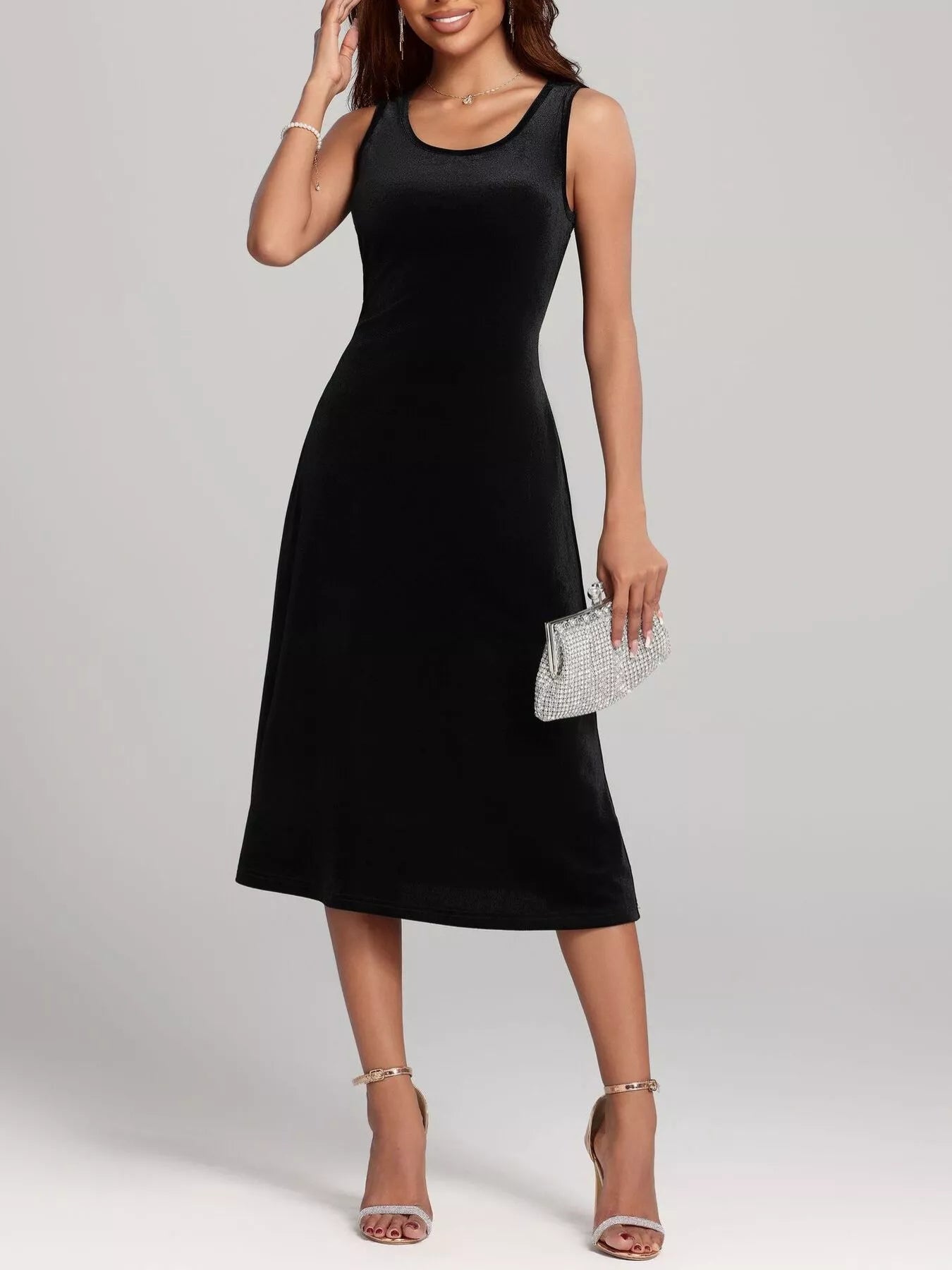 Woman wearing a black sleeveless dress holding a silver clutch against a plain background