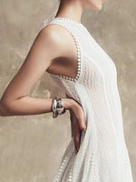 Woman wearing a white dress with a textured back design, holding her arm with a bracelet.