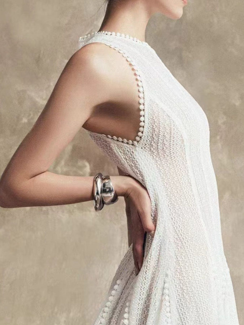 Woman wearing a white dress with a textured back design, holding her arm with a bracelet.