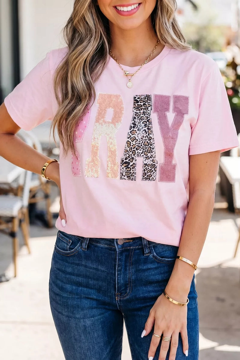 Woman wearing a pink t-shirt with colorful text design outdoors.