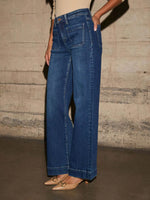 Person wearing blue jeans against a textured wall.