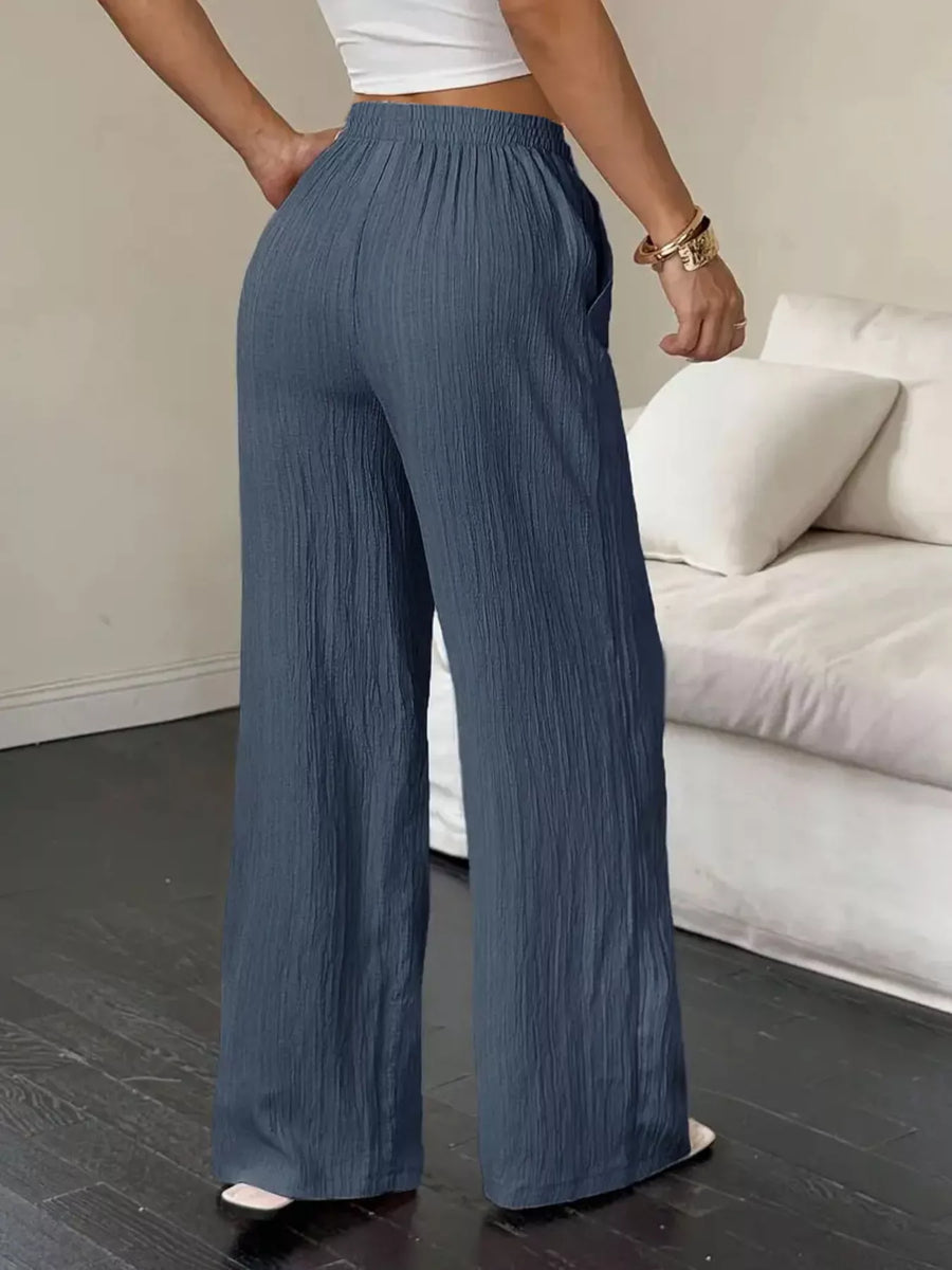 Person wearing blue wide-leg pants in a room with a white couch.