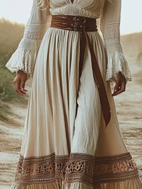 Long beige dress with lace details and a brown belt on a blurred natural background