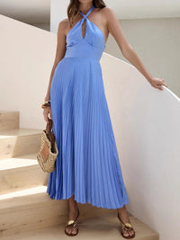 Woman in a blue pleated dress standing on wooden stairs.