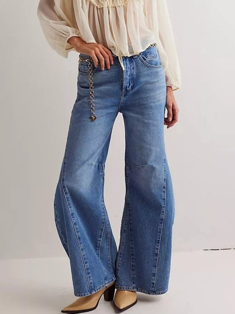Person wearing a white blouse and blue flared jeans on a plain background