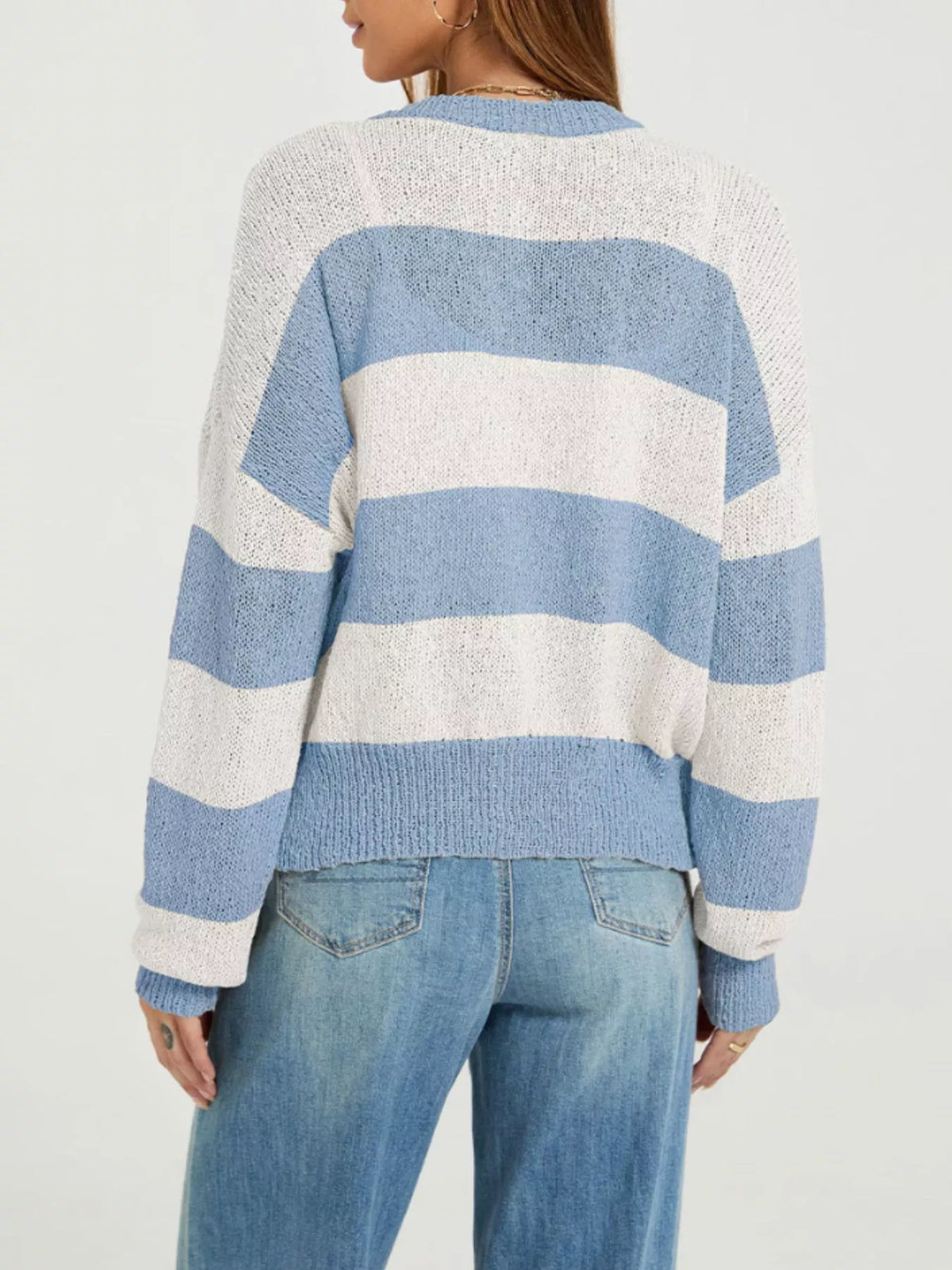 A woman wearing a blue and off-white horizontally striped knit sweater, shown from the back, paired with blue jeans against a plain light background.