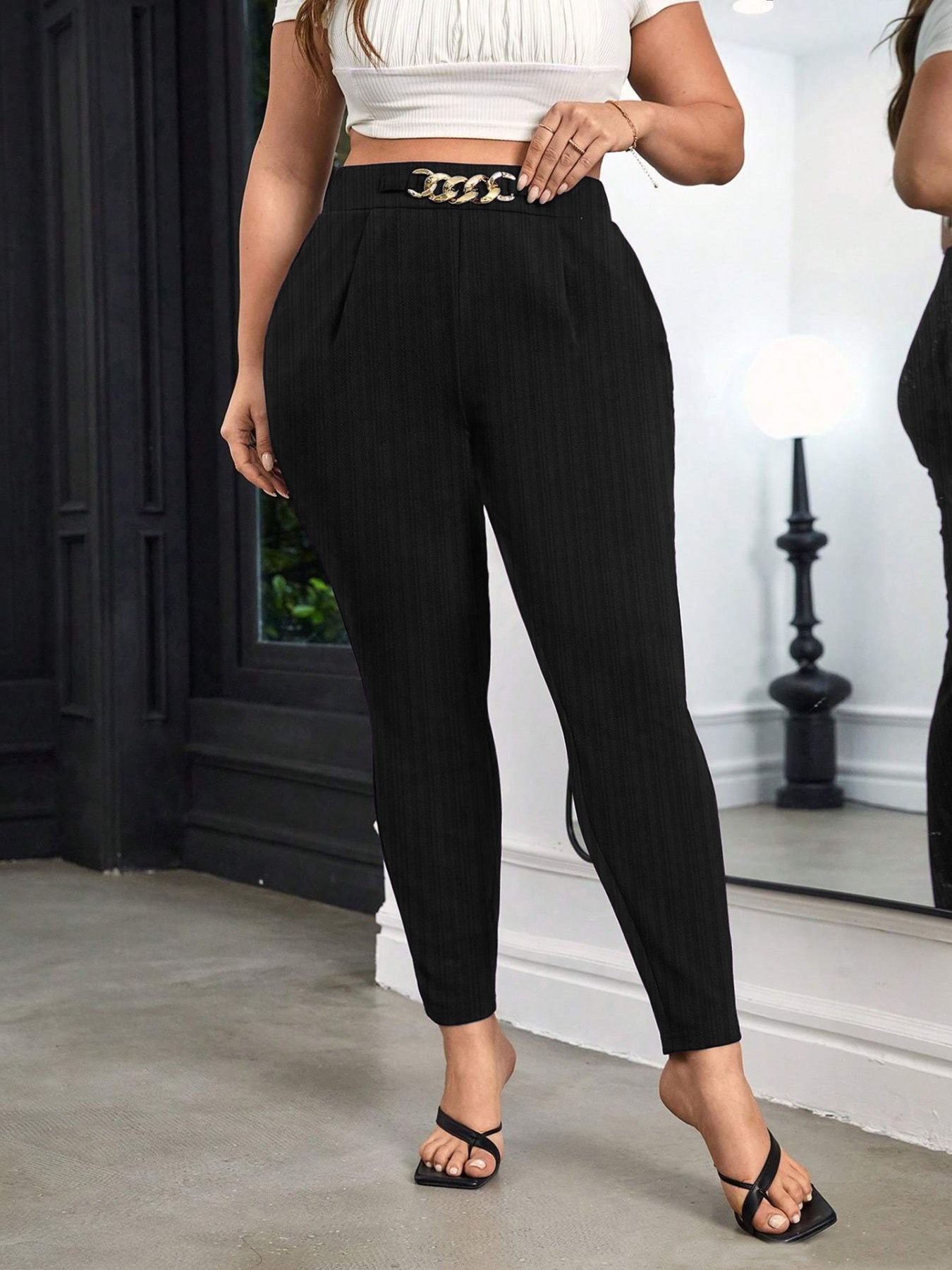 Person wearing black pants with a gold chain belt in an indoor setting