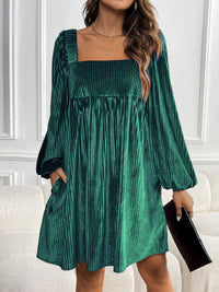 Woman wearing a green velvet dress holding a black clutch in an indoor setting.