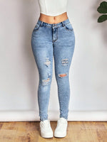 Person wearing light blue ripped jeans and white sneakers on a plain background