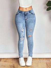 Person wearing light blue ripped jeans and white sneakers on a plain background