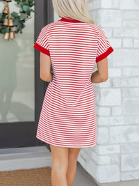 Woman wearing a red and white striped dress against a white brick wall.
