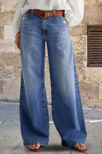 Person wearing blue jeans with a brown belt against a stone wall background