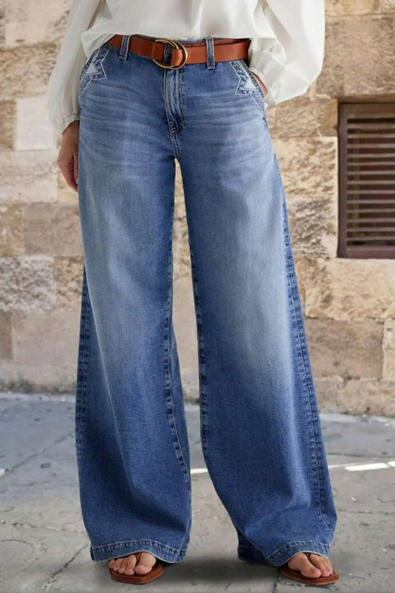 Person wearing blue jeans with a brown belt against a stone wall background