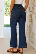 Person wearing blue jeans standing against a stone wall.