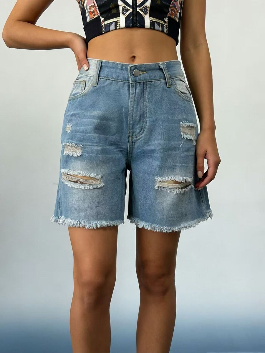 Person wearing distressed denim shorts on a plain background