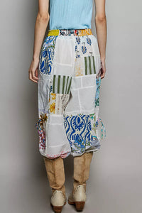 Person wearing a colorful patchwork skirt with a plain background