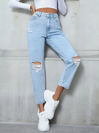 Person wearing light blue ripped jeans and white sneakers against a gray wall.