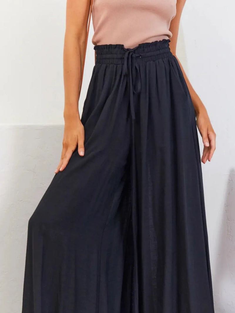 Person wearing a beige top and black wide-leg pants against a white background