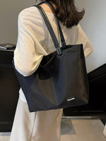 Person wearing a black tote bag with a visible brand logo indoors.
