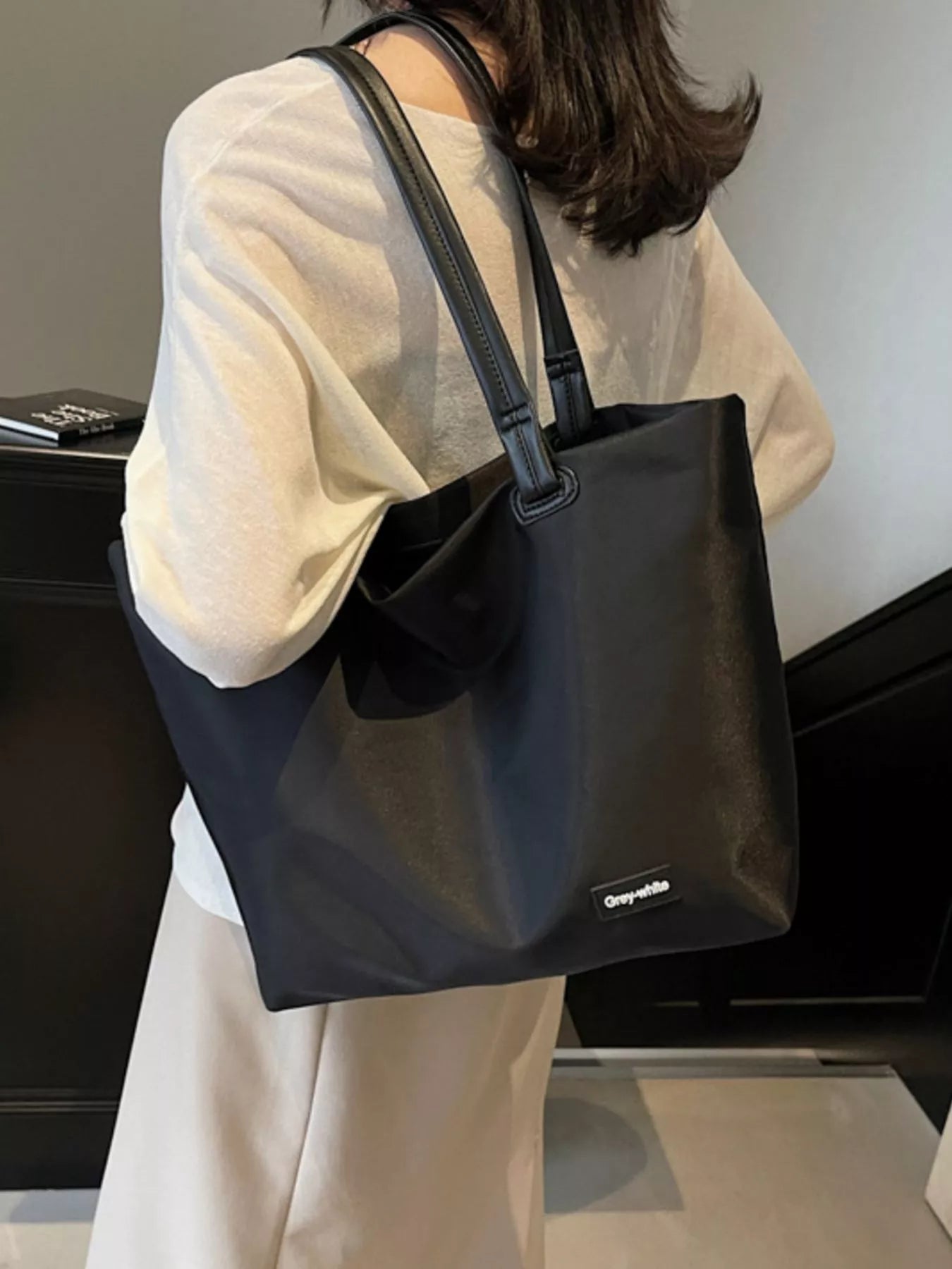 Person wearing a black tote bag with a visible brand logo indoors.