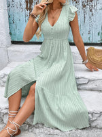Woman wearing a light green dress with ruffled sleeves and a slit, standing on stone steps.