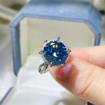 Blue gemstone ring held by a hand with a blurred background