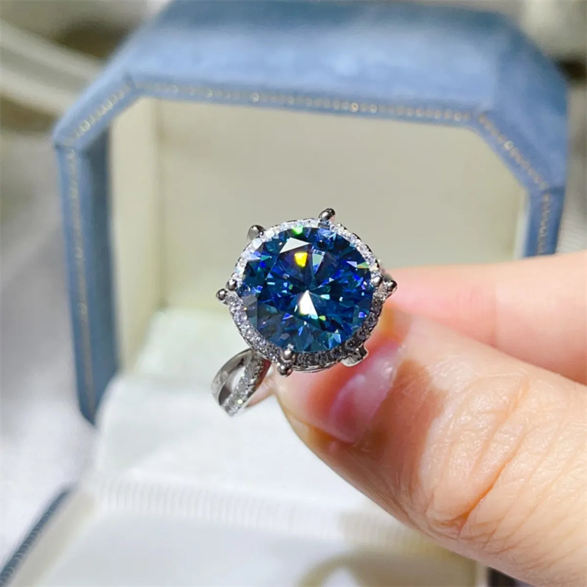 Blue gemstone ring held by a hand with a blurred background