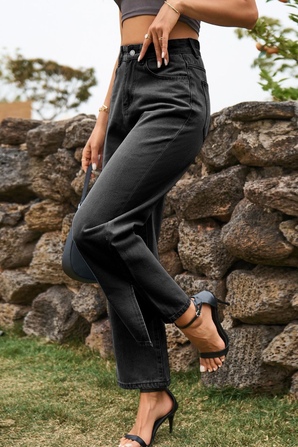 Person wearing black high-waisted jeans standing against a stone wall.