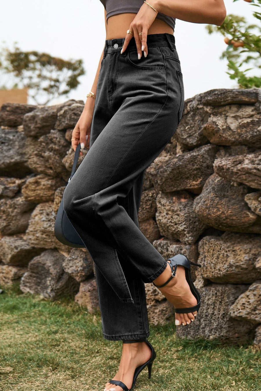 Person wearing black high-waisted jeans standing against a stone wall.