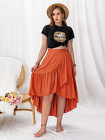 Woman wearing a black crop top with a graphic design and an orange skirt on a white background