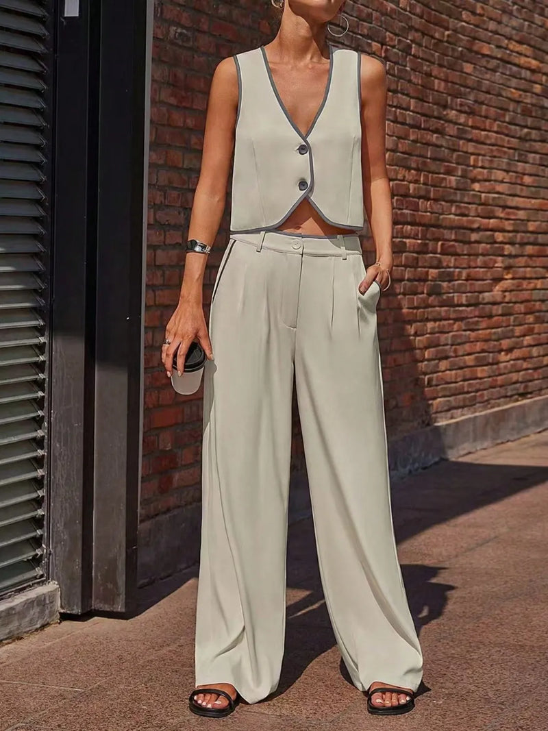 Person wearing a light gray vest and wide-leg pants standing against a brick wall.