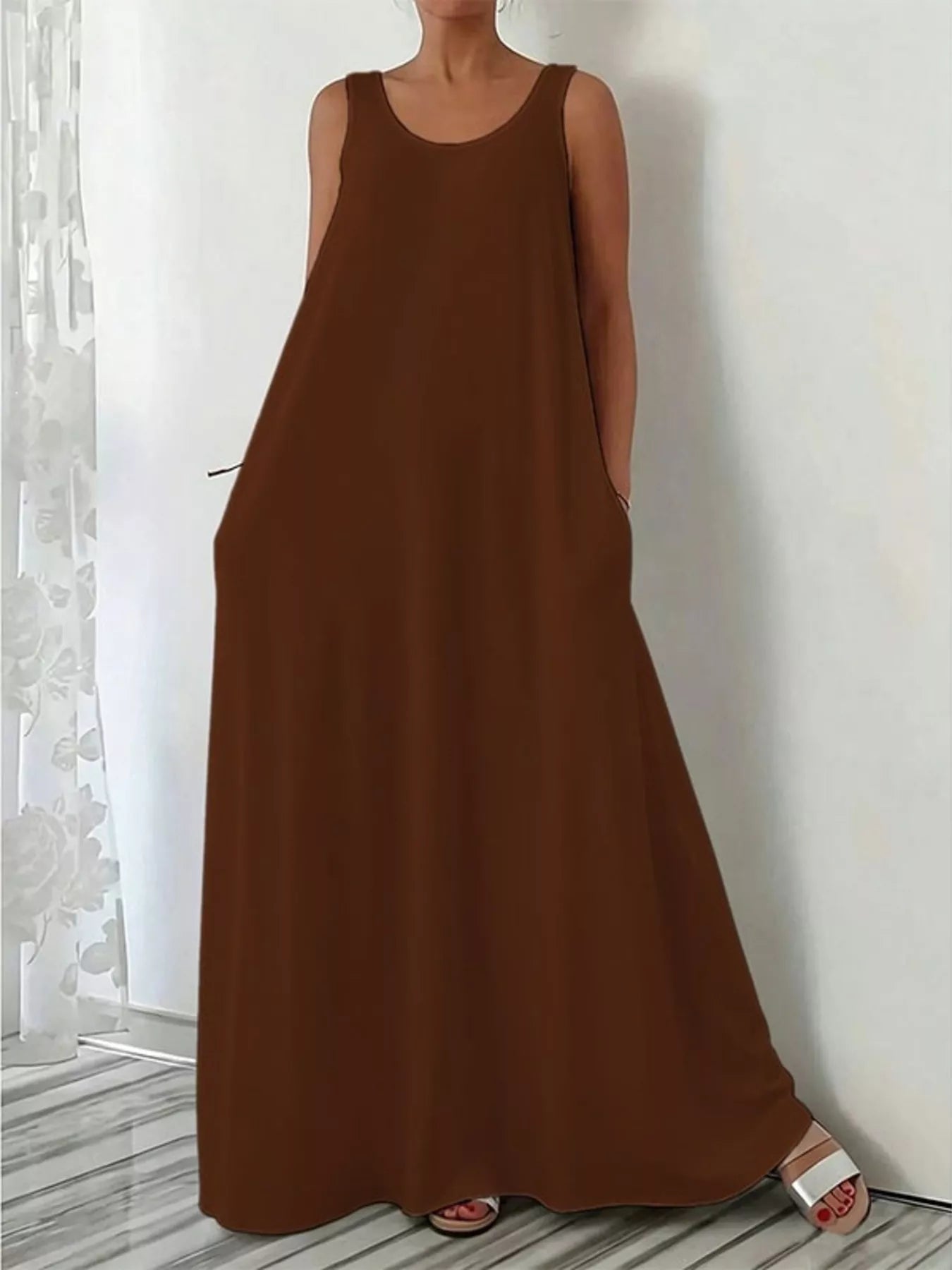 Brown sleeveless dress worn by a person against a white wall.