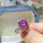 Pink gemstone ring held by a hand with a blurred background