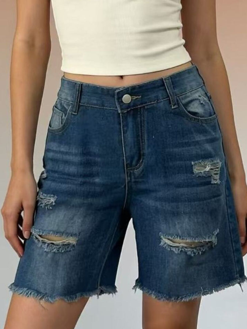 Person wearing blue denim shorts with distressed details on a plain background